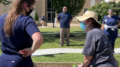 Student works with older adult planting flowers outside the Minka House