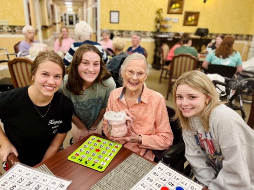 3 student volunteers playing bingo with a smiling older adult