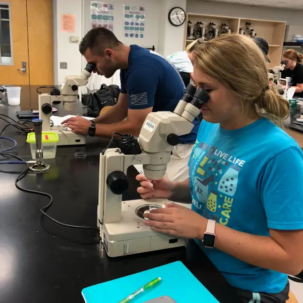 Two students use high-powered microscopes in a science lab