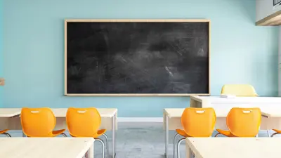 An empty classroom with chairs at tables and a blank chalkboard