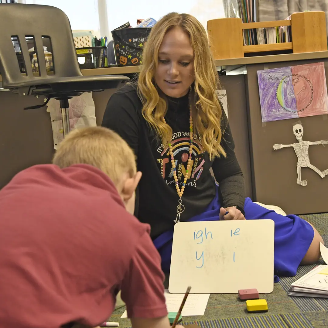 Teacher education student shows a young student what she's written on a small whiteboard