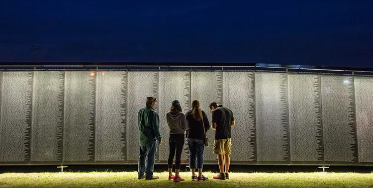 Visitors stand in front of The Wall That Heals lit up at night