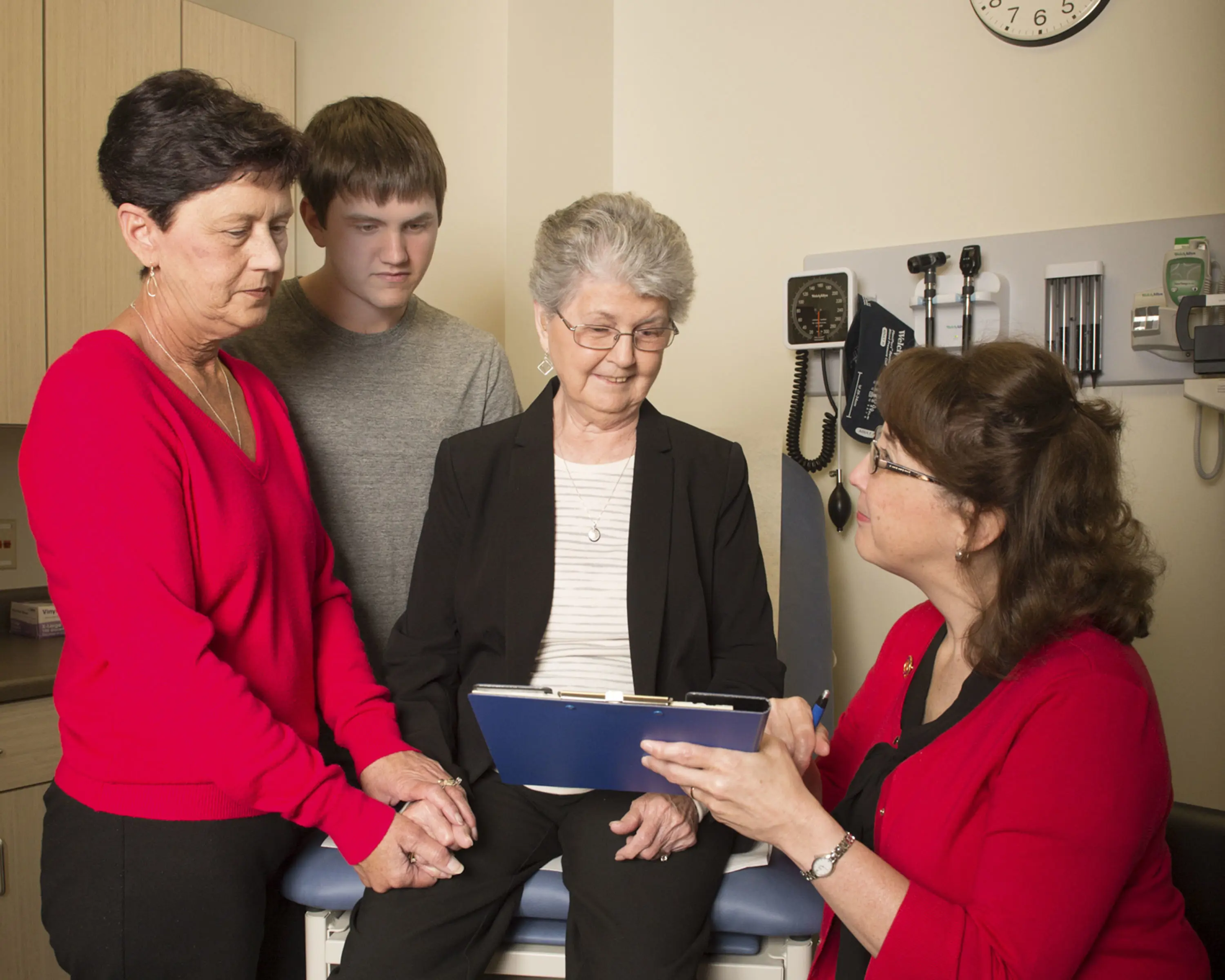 Nurse practitioner looking at medical chart with older adult, her daughter and grandson