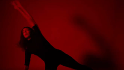 Woman does a full body stretch pose in a room lit by a red light