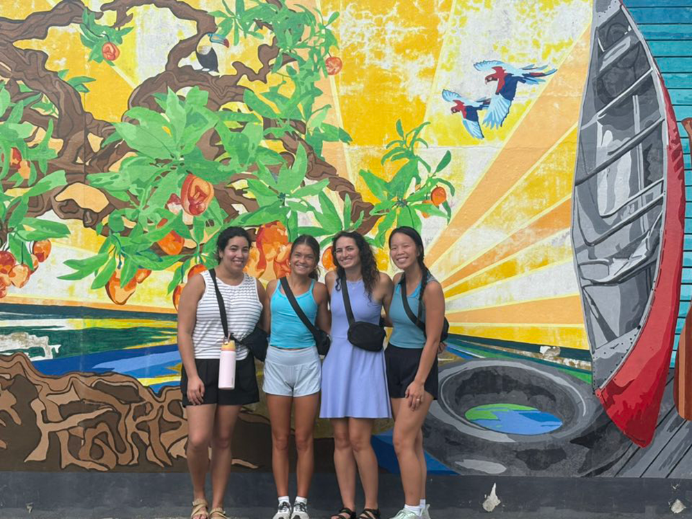 Students pose for photo in front of a mural