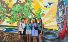 Students pose for photo in front of a mural