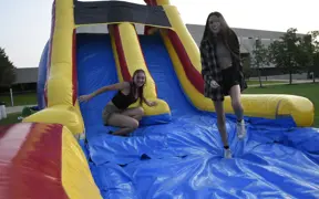 Students smile while sliding down an inflatable slide on the campus Quad