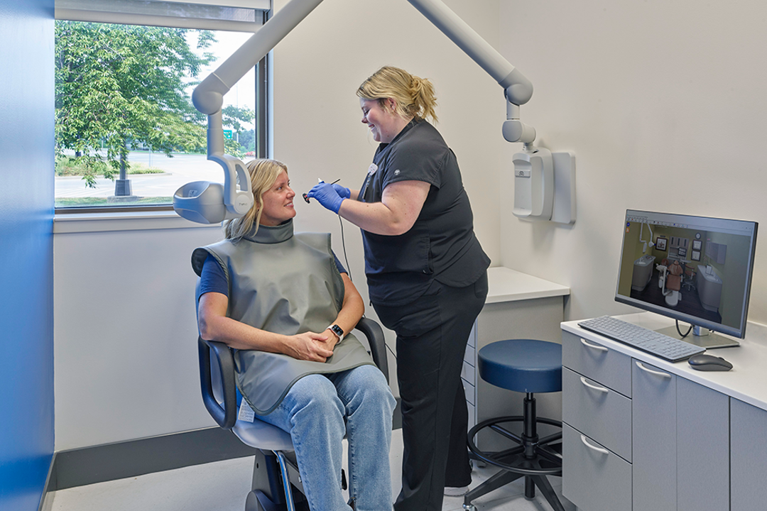 Photo of a patient in chair with a student taking a radiograph of her mouth