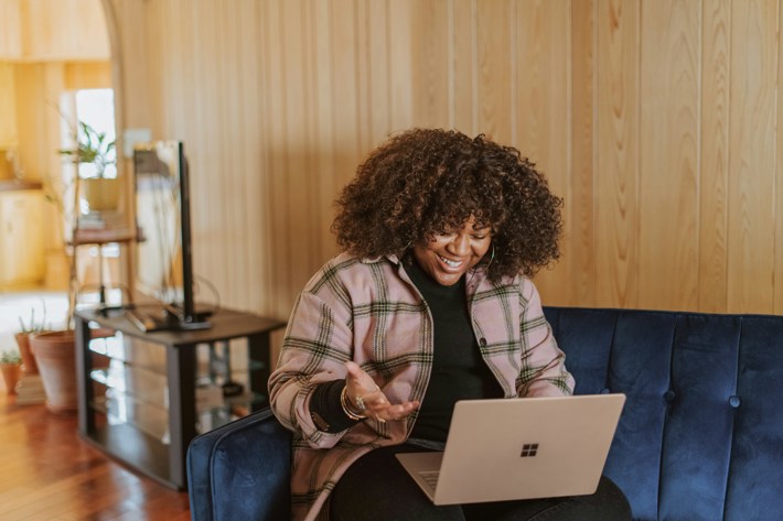 A woman smiles at her laptop from her living room