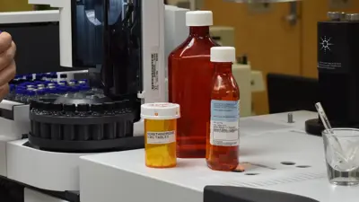 Liquid and tablet medication pharmacy bottles sit on a table near lab equipment