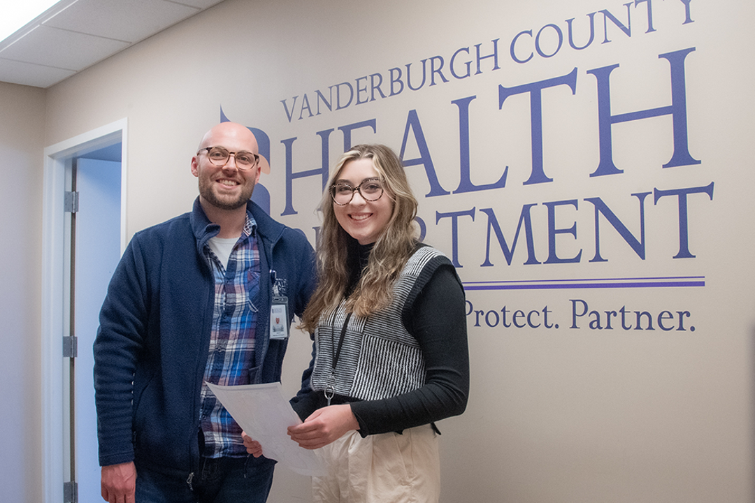 Student and employee standing in front of health department sign