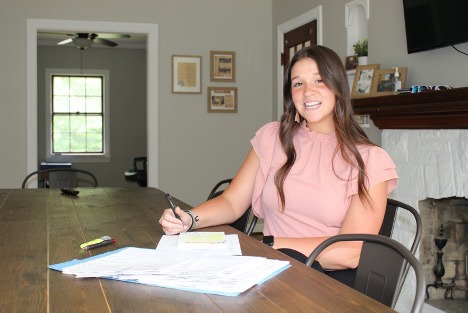 Gerontology student smiles at the camera while working on a project with pens and paper