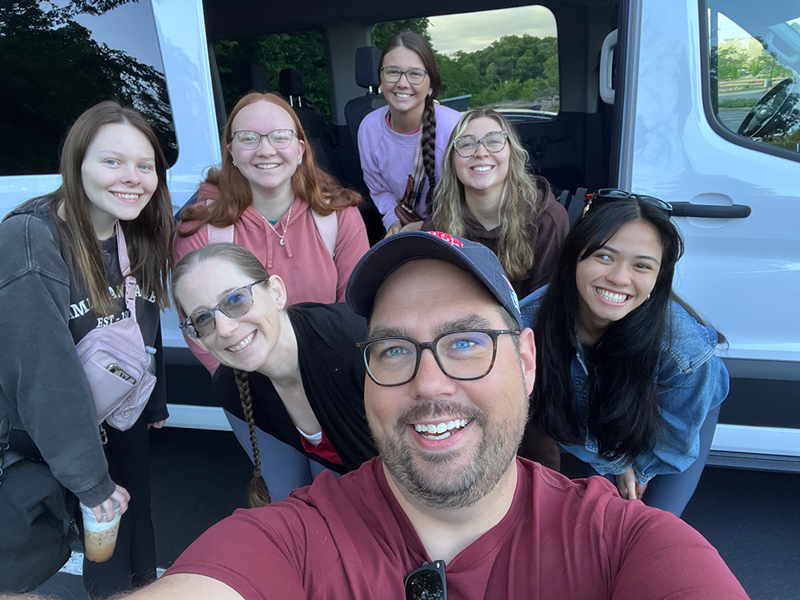 Students and faculty pose for selfie in front of a van