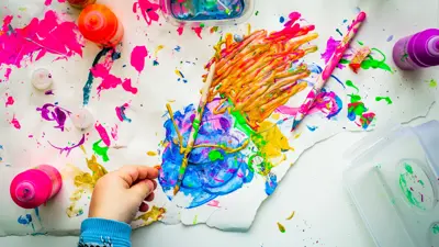A first-person perspective view of an art table smeared with brightly colored paint