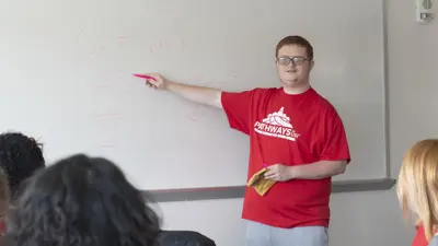 Student in a Pathways to USI t-shirt explains a math problem at the whiteboard