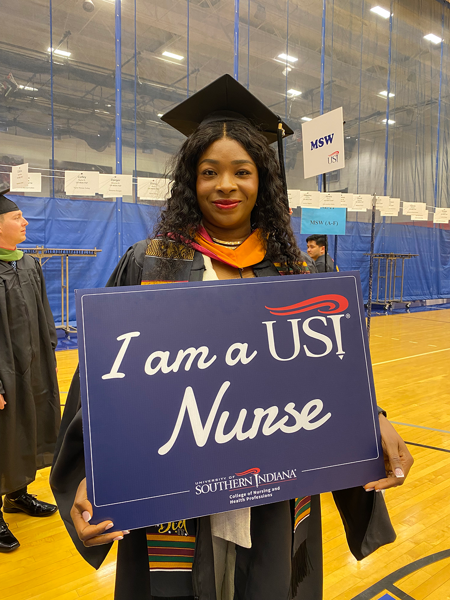 Master of Science in Nursing student in cap and gown holding "I am a USI Nurse" sign