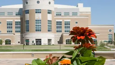 An exterior view of the Rice Library from across the Quad, with a flower in the foreground