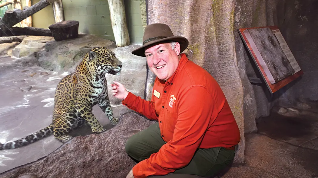 man in jungle hat sitting next to jaguar