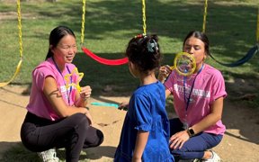 OT students blowing bubbles with child next to swingset