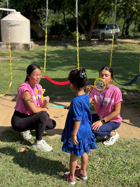 OT students blowing bubbles with child next to swingset