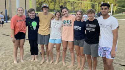 Group of students smile and pose on the campus sand volleyball court