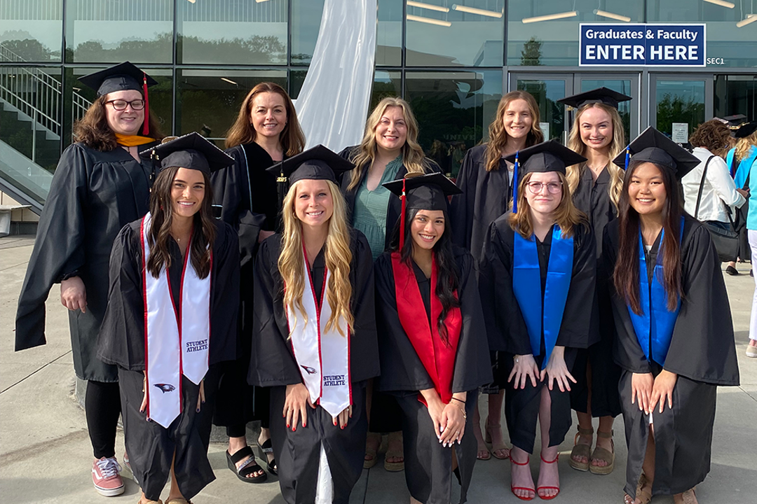 Food and nutrition faculty and students in their commencement regalia posing outside the Screaming Eagles Athletics Complex