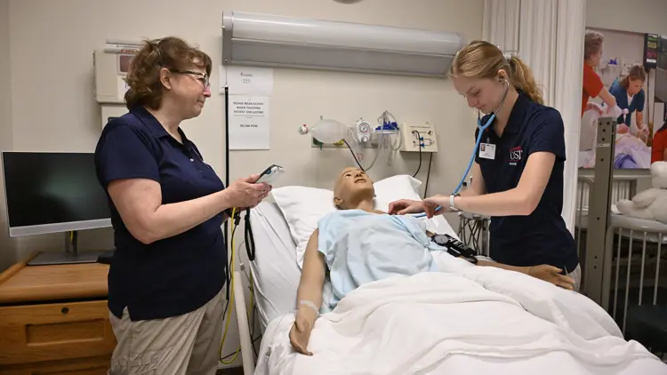 Faculty member with student in a hospital room with a simulation patient