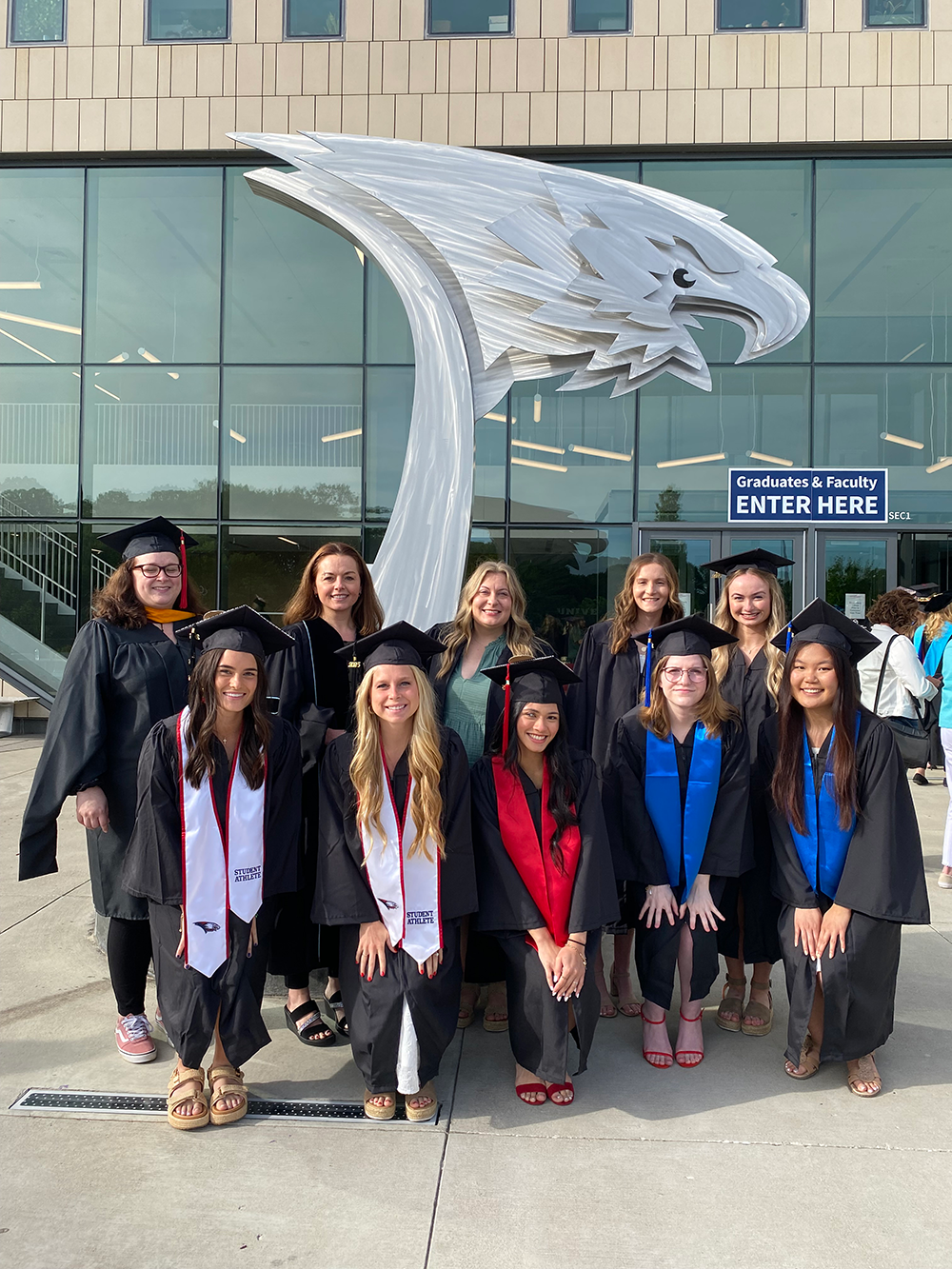 Food and nutrition students and faculty in graduation regalia standing outside in front of arena
