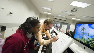 Student sits at a keyboard while music faculty assist with sheet music