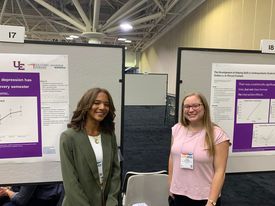 Two USI students in professional attire pose in front of their posters at a conference