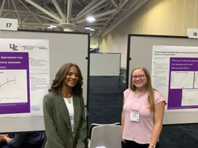 Two USI students in professional attire pose in front of their posters at a conference