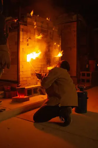 A student crouches next to a fiery kiln in the ceramics studio