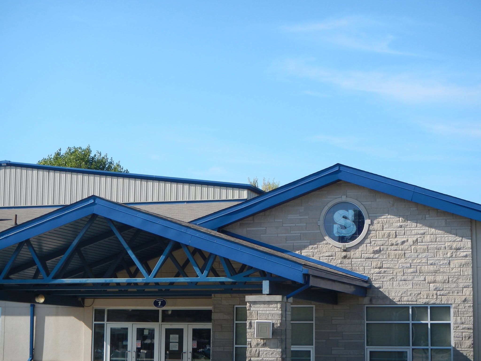 Exterior view of the SCA school building with a blue roof and main entrance on a clear day.