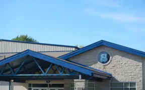 Exterior view of the SCA school building with a blue roof and main entrance on a clear day.