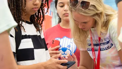 USI Welcome Week volunteer helps a new student find something on her cell phone