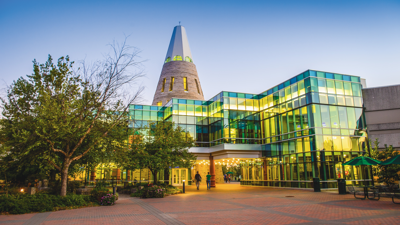 A view of the University Center, including the Tower, at dusk with the lights on green trees