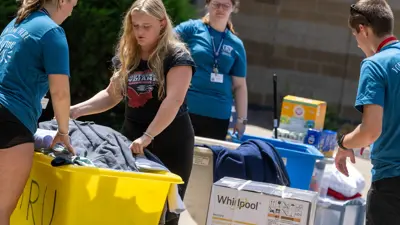 Housing and residence life staff help a student move her belongings into a residence hall in a big bin