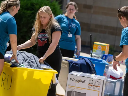 Student volunteers helping a new student put items into cart at move in.