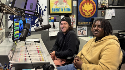 Two male students smile at the camera from behind the soundboard in the USI campus radio studio