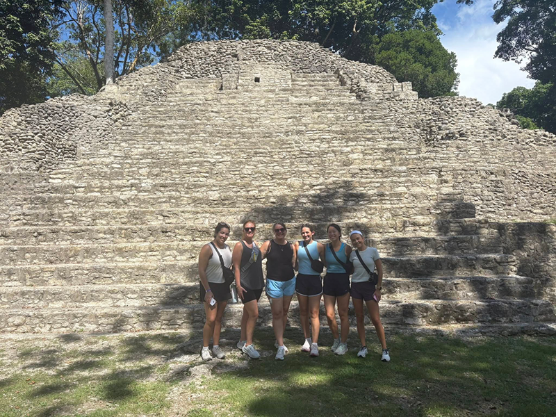 OT students and a faculty member pose for photo in front of a wall