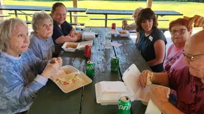Older adults have lunch at at outdoor picnic table