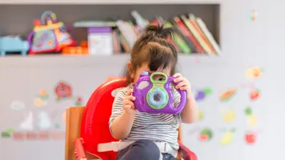 Small child sits in a high chair using a toy camera