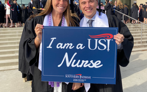 Two nursing students in caps and gowns holding "I am a USI Nurse" sign