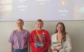 Three students pose for photo in front of a screen