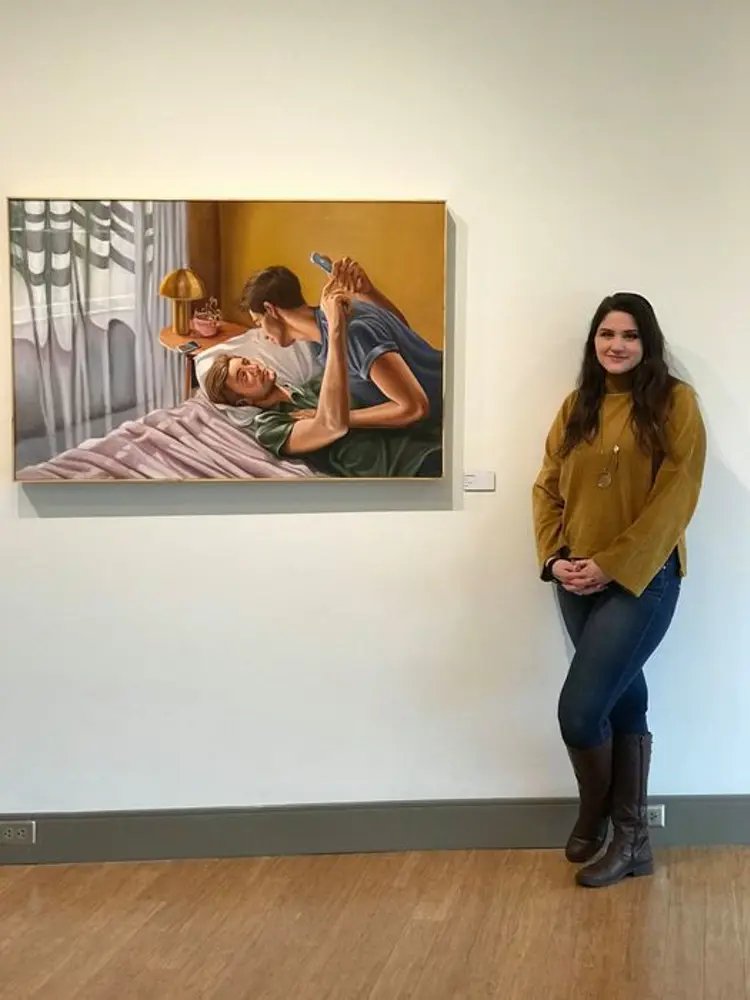 Photo of artist next to a painting of two people laying down