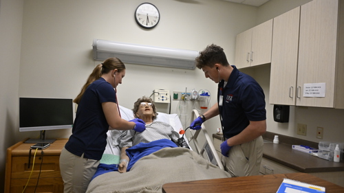 Two nursing students helping an artificial patient in a hospital setting