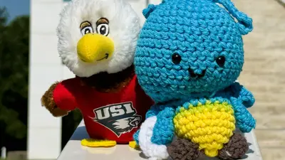 Plush blue crocheted firefly toy beside a USI eagle mascot plush wearing a red shirt.