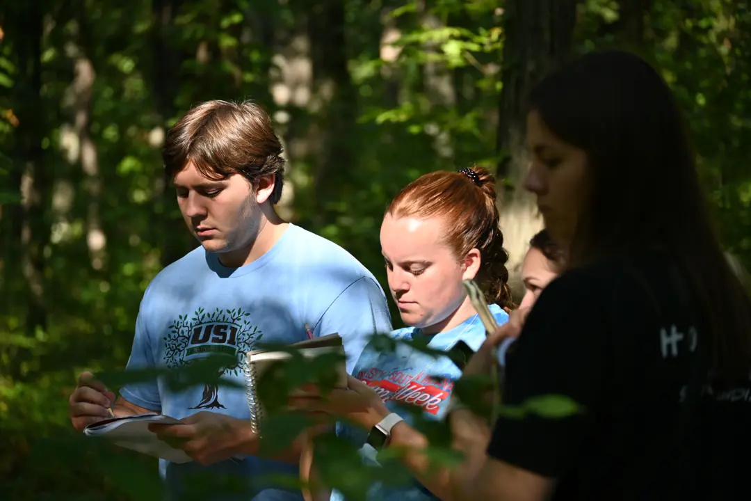 Biology students take notes in an outdoor study in a wooded area