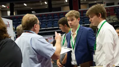 Students in professional attire speak to an employer at a career fair