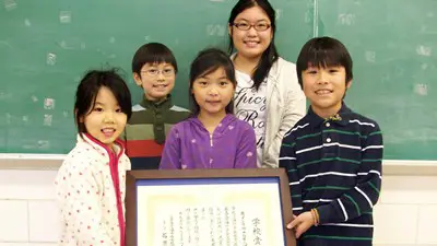 A group of elementary school children pose with a framed document in Japanese